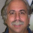 Man smiling with a mustache, wearing a dark shirt.