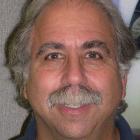 Man smiling with a mustache, wearing a dark shirt.