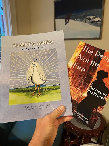 A person holding two books, one with a drawing and another with a flame illustration.