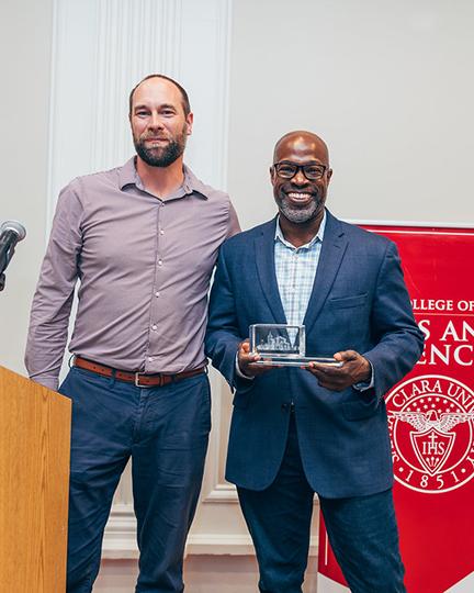Kafui Dzirasa holding his speakers plaque next to Brian Bayless at a recognition dinner 