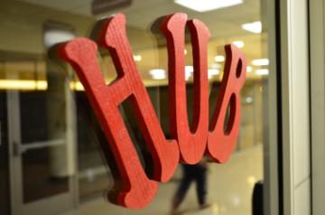 Red Hub sign on glass with room and person in the background. 