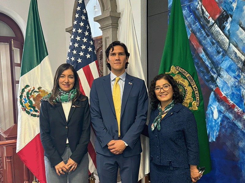 Octavio De Leon standing with two women in front of flags