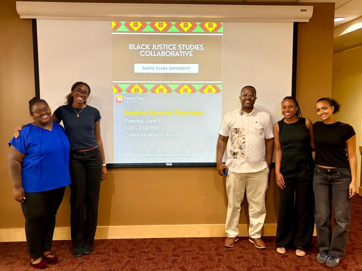 Students and a professor pose in front of a projector screen with an event flyer