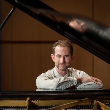 A person posing with arms crossed behind a grand piano.