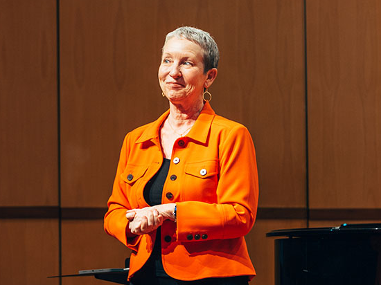Teresa McCollough standing on stage wearing an orange jacket.