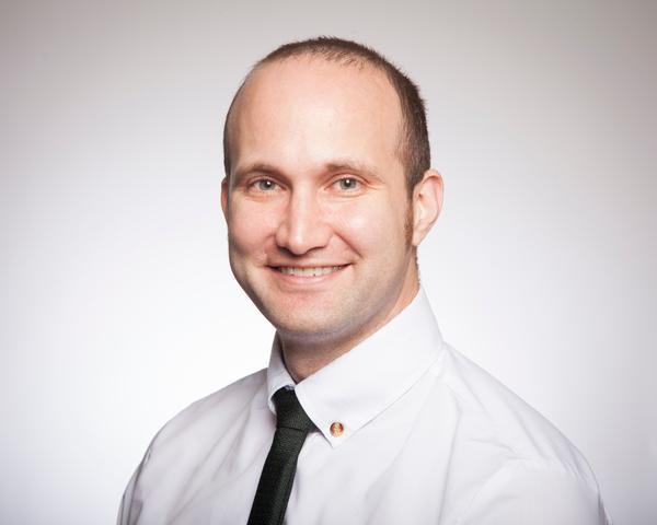 A person in a white shirt and black tie smiling.