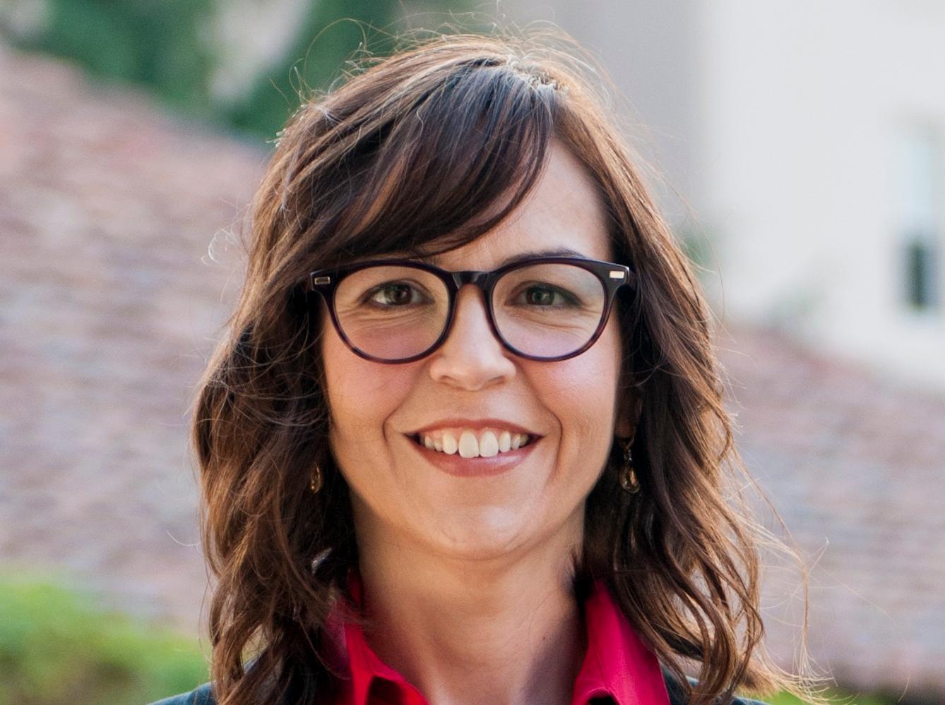 A person wearing glasses, a red shirt, and a black blazer.
