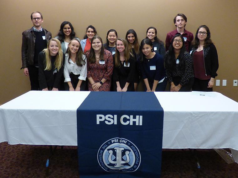 Group photo of individuals standing behind a Psi Chi table.