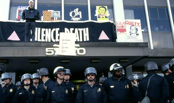 Police officers standing beneath balcony with protest signs reading DEPLOY FDA and S.O.S.