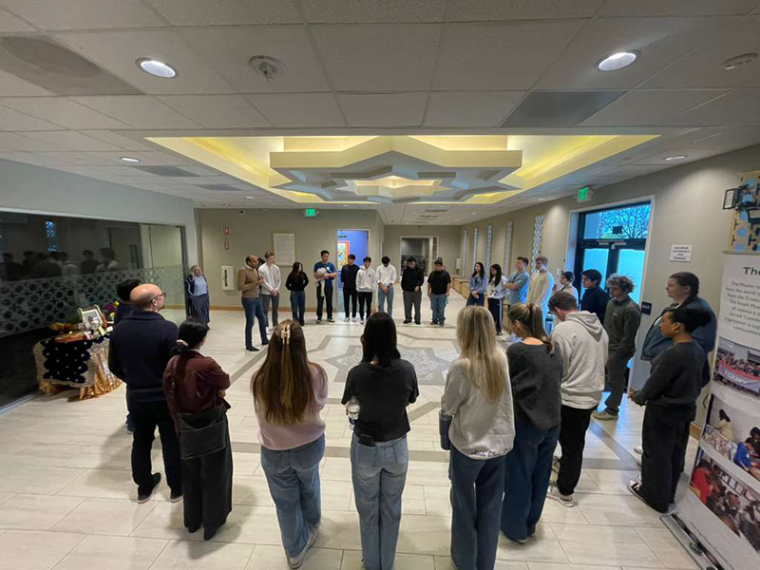 Faculty and students stand in an oval taking in a talk.