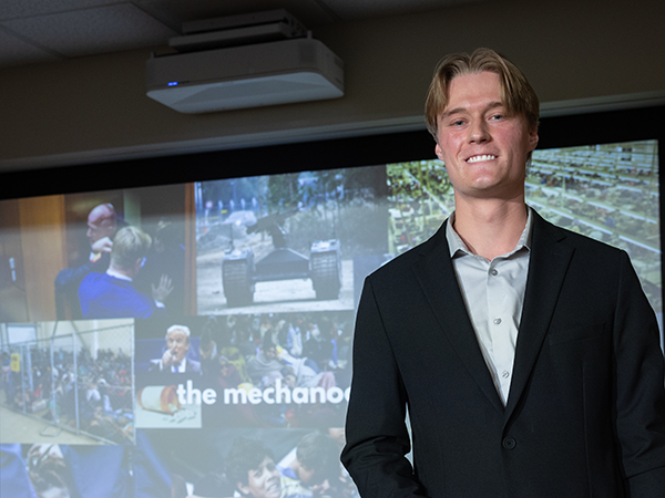 Gavin Brunsman ’27 standing in front of the screen projection of his presentation