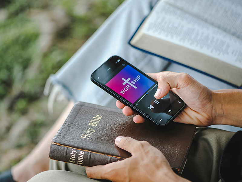 Hands holding a bible and cell phone with worship mobile app displayed