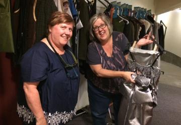 Two people smiling while inspecting costumes on a rack. 