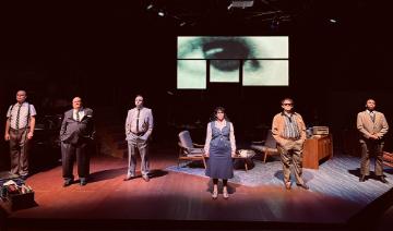 5 men and a woman standing on a stage set with an eye projected on a screen in the background