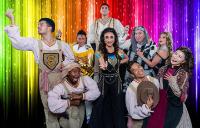 Joseph and the Amazing Technicolor Dreamcoat cast in front of a rainbow shimmer backdrop