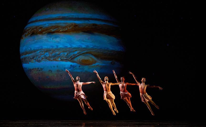 4 ballerinas jumping in cabriole against a projection of Jupiter