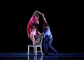 A man in blue lifting a woman in pink over the back of a white wooden chair