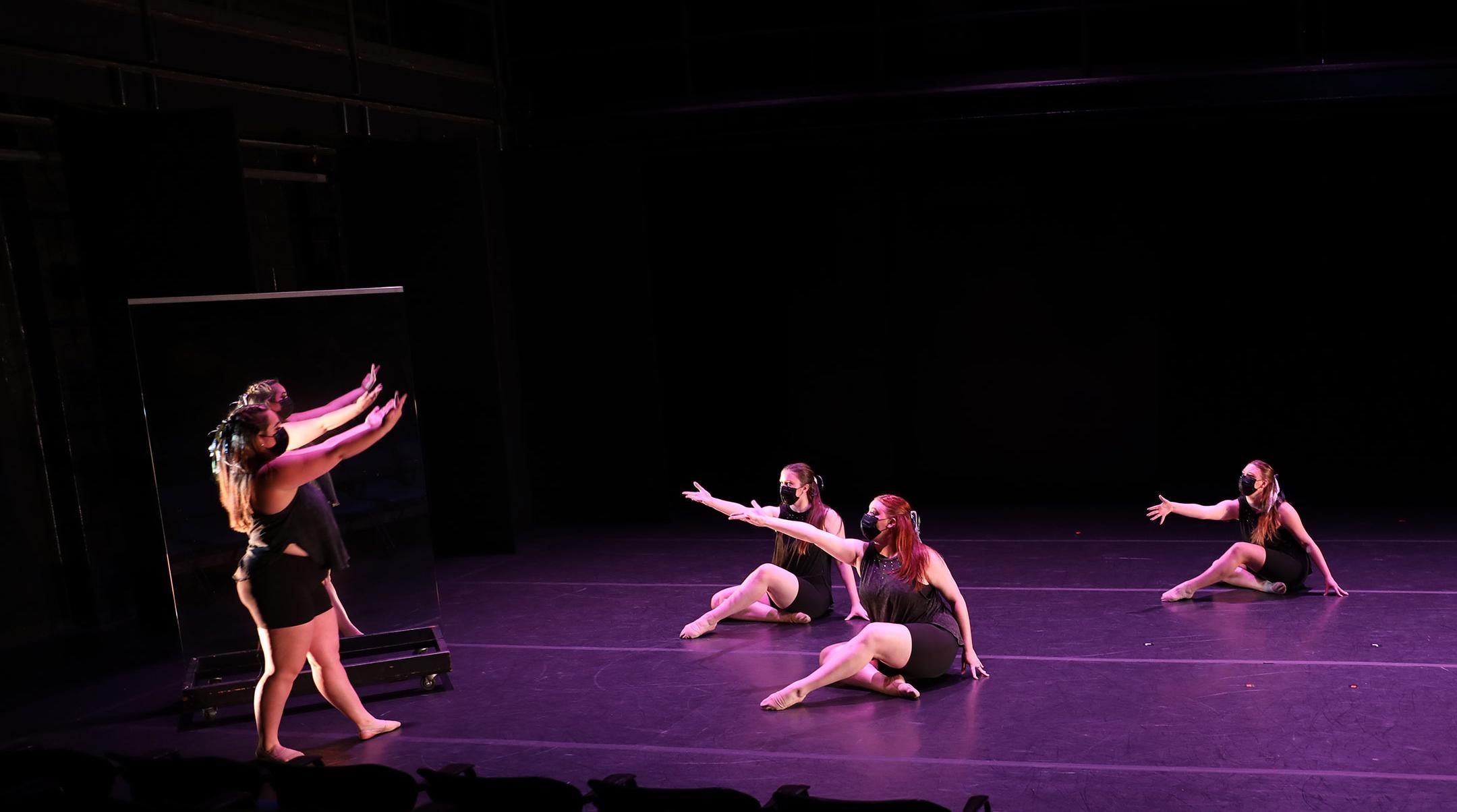 4 female modern dancers 1 in front of a mirror 3 seated with R arm outstretched