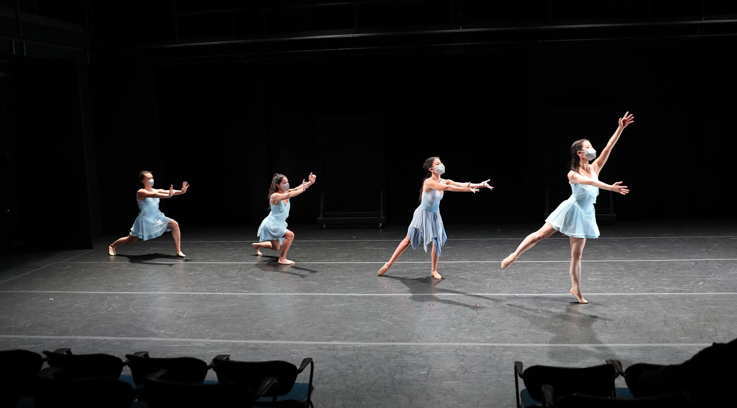 4 female modern dancers in a diagonal line wearing blue dresses