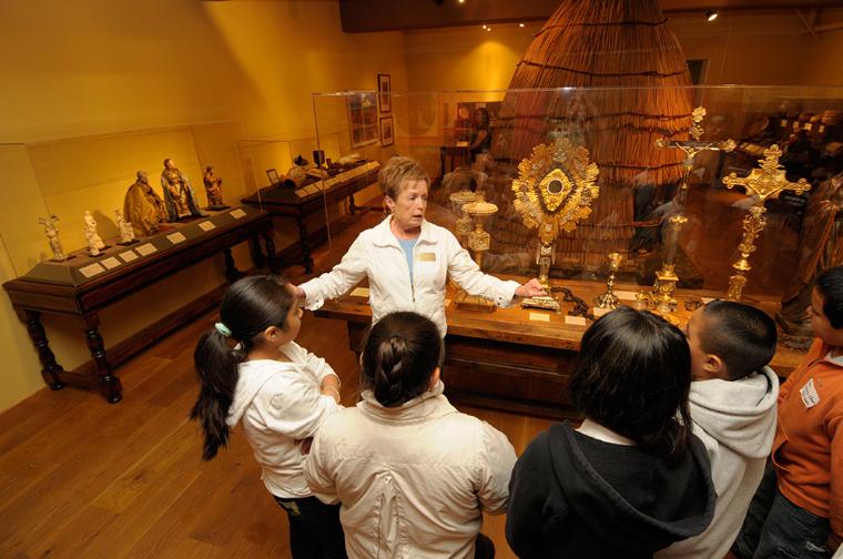 California History docent giving a tour of the museums mission exhibit to school children.