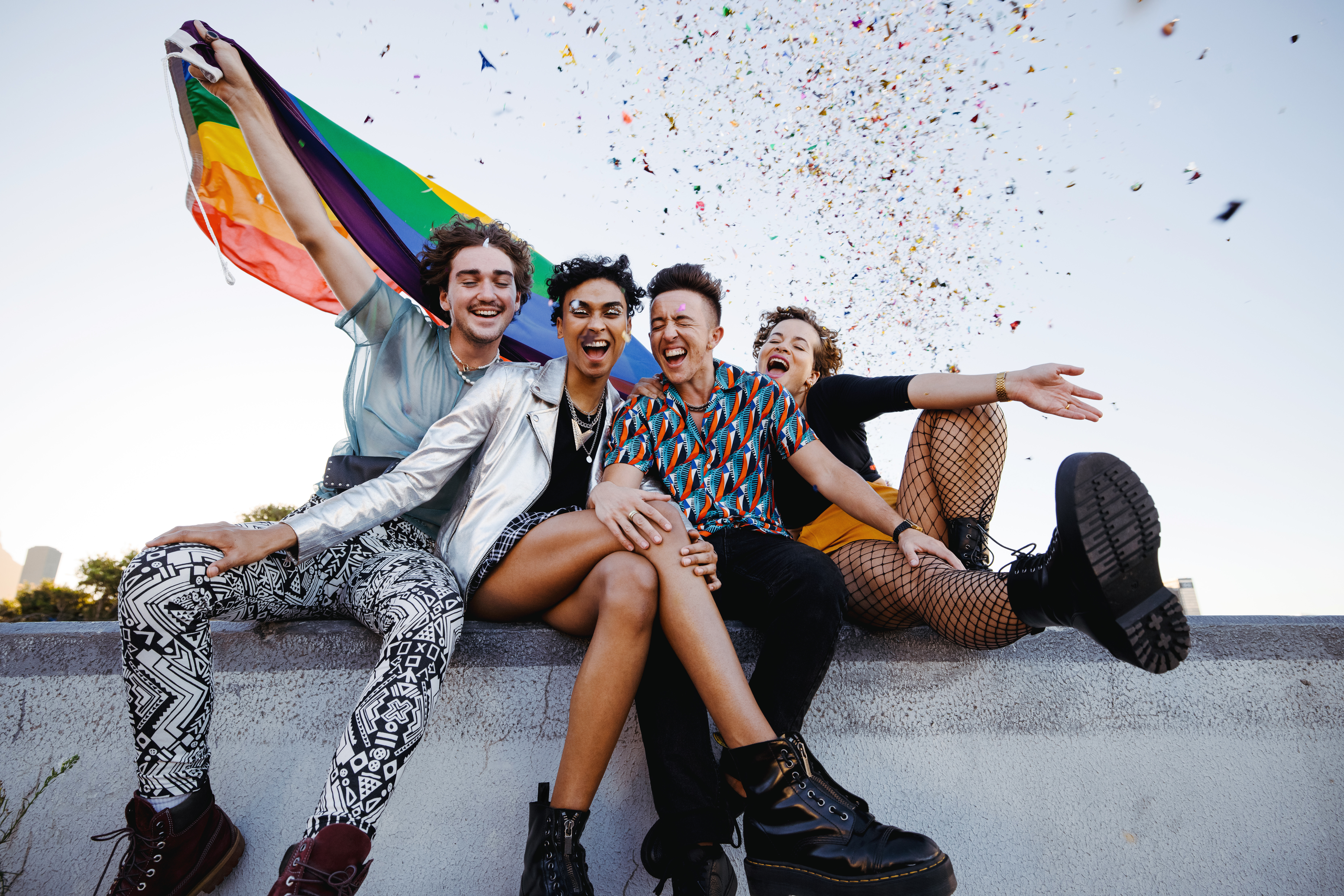 Group of friends holding a pride flag with confetti in the background.