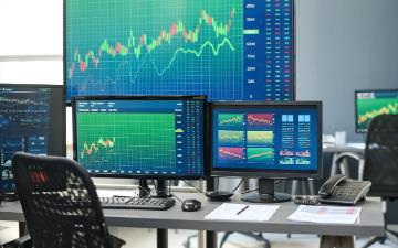 Stock and currency trading agents workspace with desktop computers and various monitors in modern office interior. Photo by pressmaster via Adobe Stock.