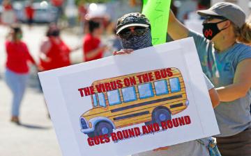 a person wearing facemask and carrying a sign with an image of a school bus and slogal