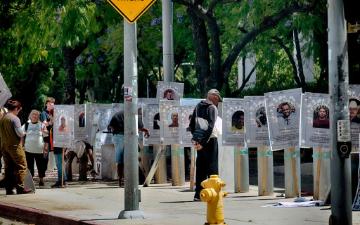 A pedestrian stops to look at a line of photos of people who died while in detention in front of the Federal Building in downtown Los Angeles on Monday, May 4, 2026. (AP Photo/Richard Vogel)