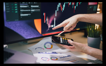 Falls and rises of the stock exchange displayed on a computer monitor. A person holding a calculator in one hand points at the screen from another. Image by Jakub Zerdzicki on Pexels and created via Canva Enterprise.