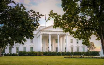 A large white house with columns and many windows. The house sits on a expansive green lawn with a large circular fountain and is framed by two green leafy trees. By Ana Lanza on Unsplash.