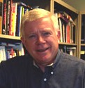 A person smiling in front of a bookshelf.