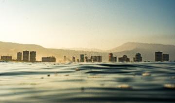 Trash in body of water with a cityscape in the background. 