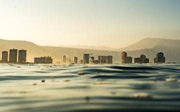 Trash in body of water with a cityscape in the background. Photo credit: Emiliano Arano/Pexels 