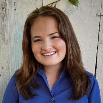 A person smiling in front of a wooden wall with leaves.