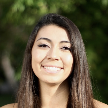 A person smiling outdoors, with long hair and a green background.