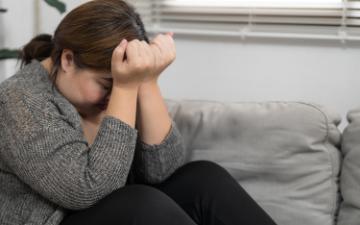 A woman sitting with her head down and covered by her hands. By Charlie's via Adobe Stock