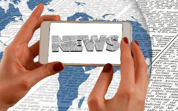 A person holding a phone displaying news text.