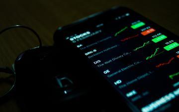 A smartphone displays stock market data with graphs and charts.