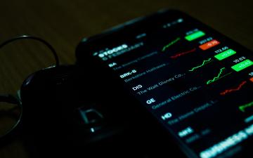 A smartphone displays stock market data with graphs and charts.