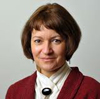 A person wearing a formal outfit and smiling against a plain background.