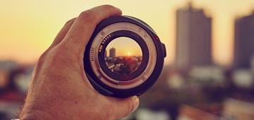 A person holds a camera lens to view the setting sun.
