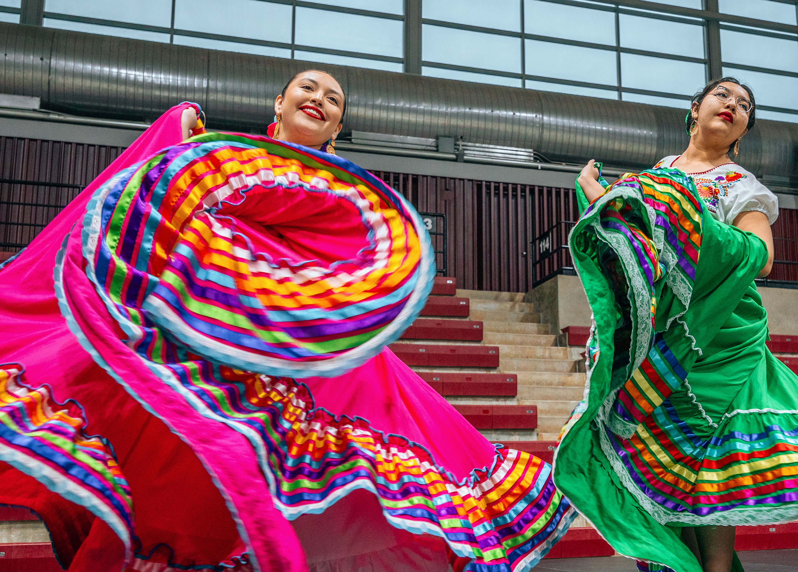 Two folklorico dancers whip their color dresses while dancing