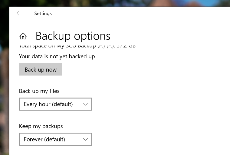 An image of the Windows 10 Backup Options page with a red arrow pointing to the Back up my files option which is set to Every hour (default)