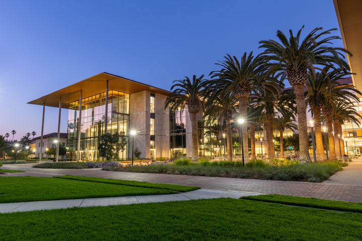 Modern building with glass walls and a spacious lawn at twilight.