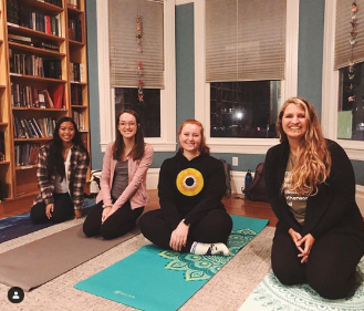 Four people sitting on yoga mats in a cozy room.