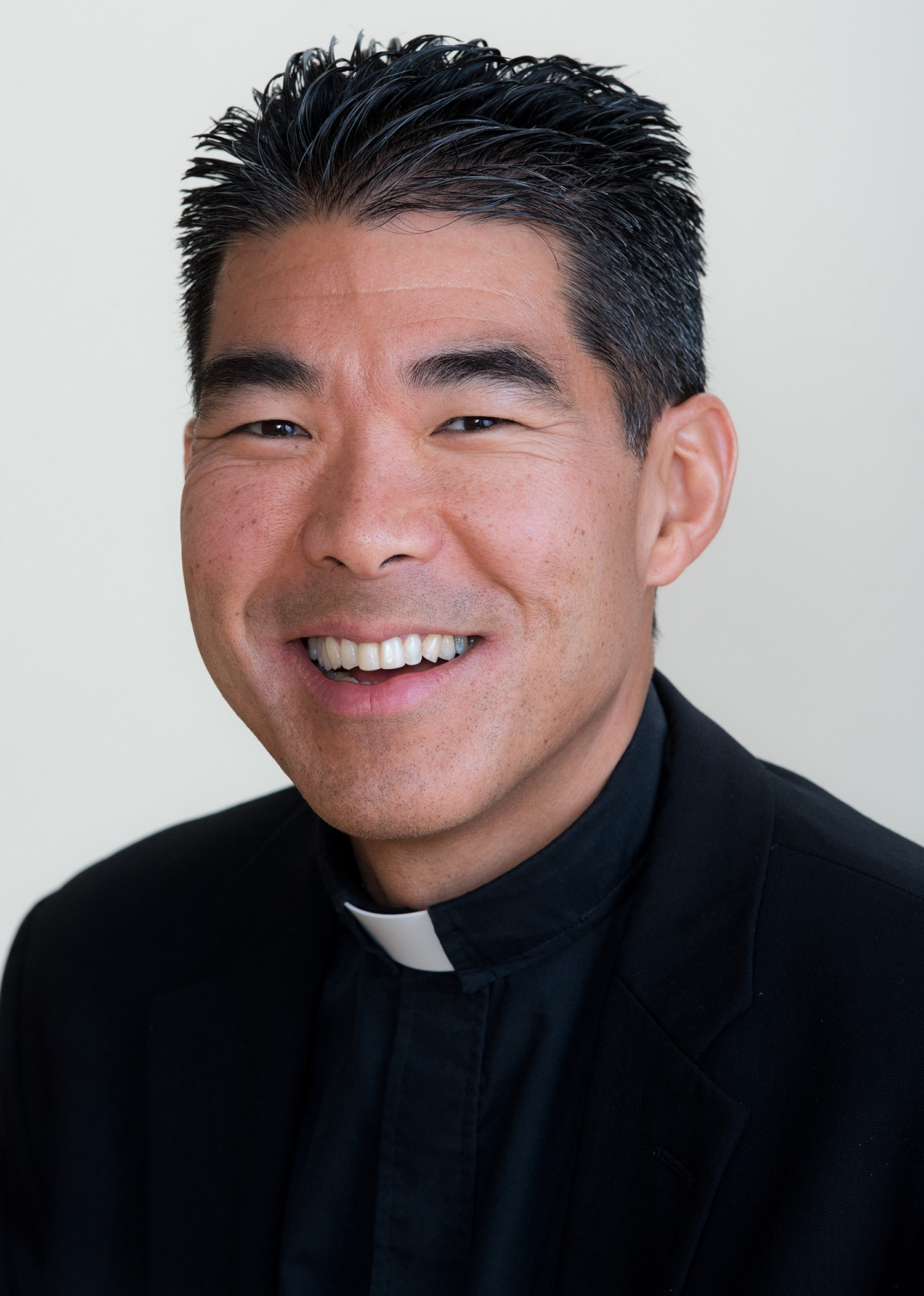A clergyman smiling with a white background.