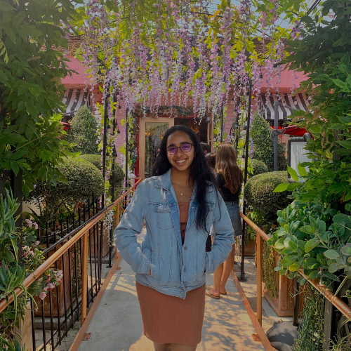 A person standing on a flower-decorated bridge in an outdoor garden.