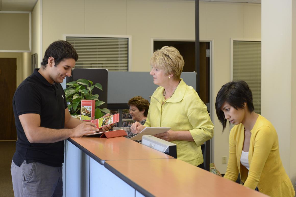 People interacting at a front desk in an office setting.
