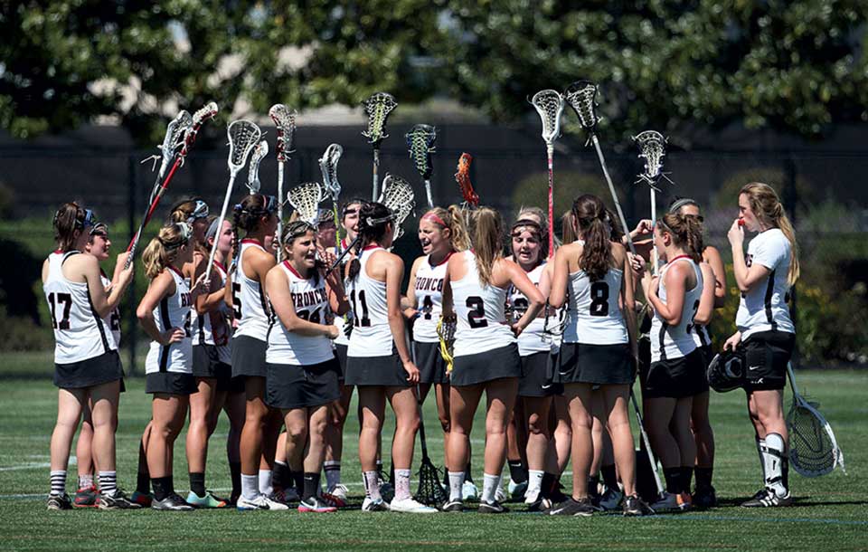 Womens lacrosse team huddled together on a field.
