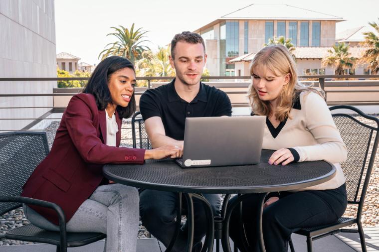 Three staff members working together on a computer at a table outside on campus. 
